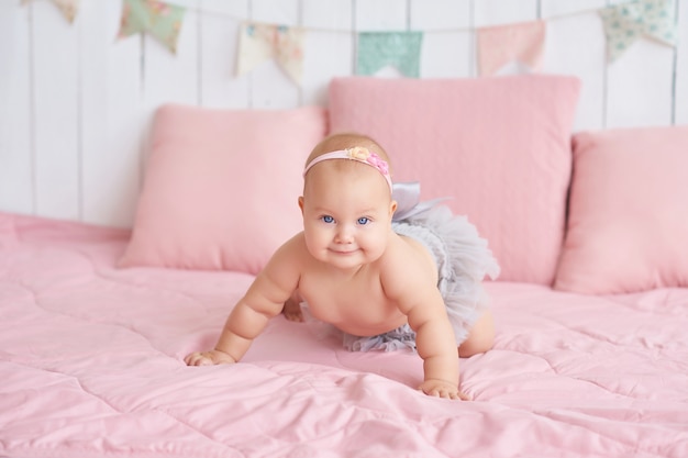 Dulce bebé gracioso en la cama en la habitación de los niños. Linda niña de 6 meses sentada y gateando.