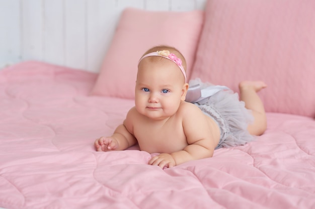 Dulce bebé gracioso en la cama en la habitación de los niños. Linda niña de 6 meses sentada y gateando.