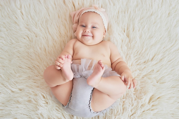 Dulce bebé gracioso en la cama en la habitación de los niños. Linda niña de 6 meses sentada y gateando.