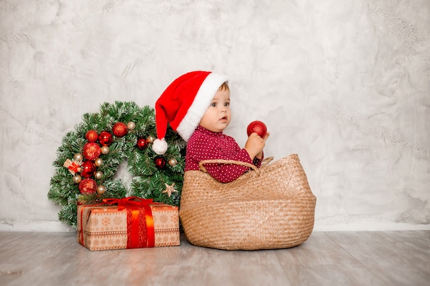 Dulce bebé Santa se sienta en una canasta de mimbre con una caja de regalo