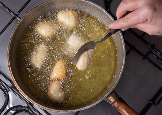 Dulce brasileño llamado bolinho de Chuva, puesto a freír en una sartén con aceite, enfoque selectivo.