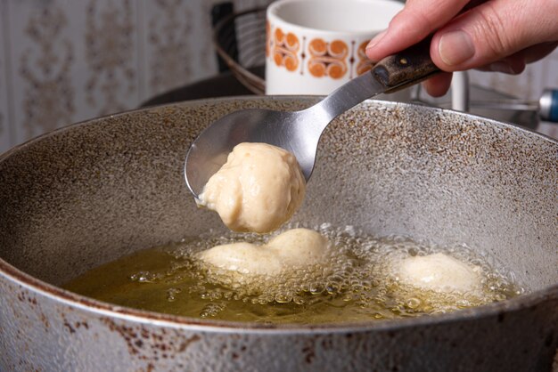 Dulce brasileño llamado bolinho de Chuva, puesto a freír en una sartén con aceite, enfoque selectivo.