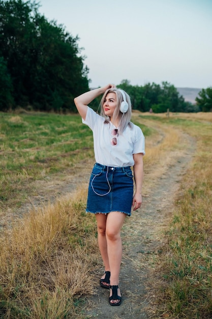 Una dulce joven feliz alegre bonita mujer caminando al aire libre en el parque en un hermoso día de verano La chica escucha música con auriculares