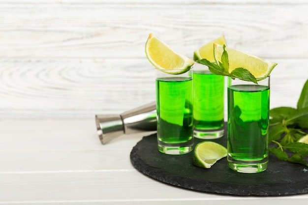 Dulce licor de menta refrescante con hielo y hojas de menta sobre el fondo de la mesa Chupitos con rodaja de lima y menta plana