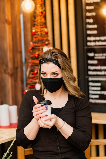 Una dulce mujer de apariencia caucásica con una mascarilla negra, se sienta y trabaja en un cibercafé