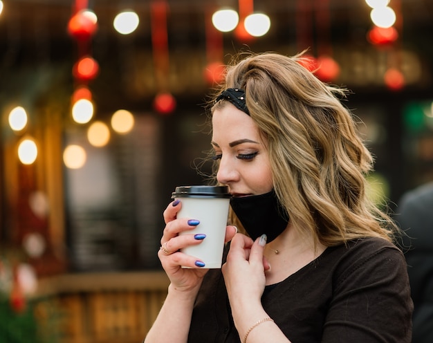 Una dulce mujer de apariencia caucásica con una mascarilla negra, se sienta y trabaja en un cibercafé.