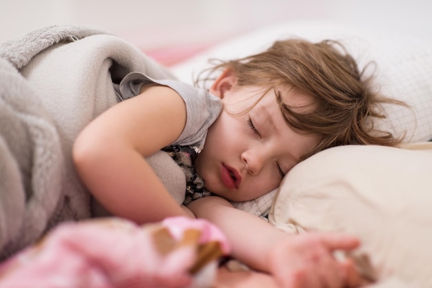 Dulce niña cubierta con una manta durmiendo en la cama en casa