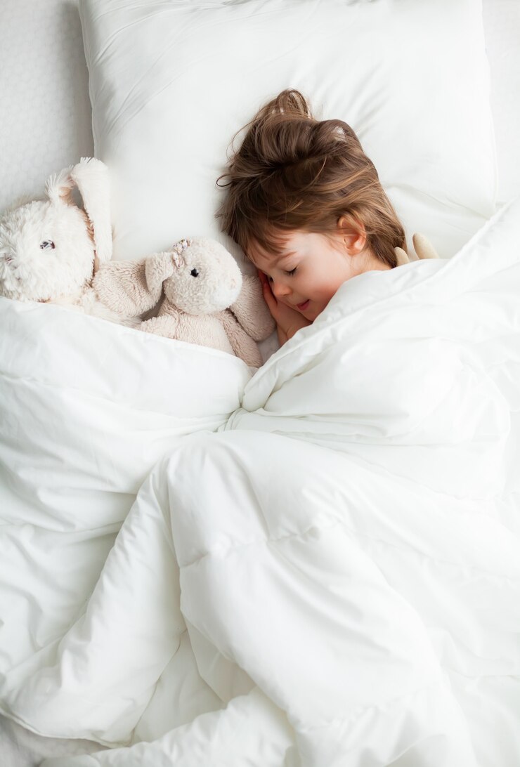 Dulce niña durmiendo en la cama blanca con juguetes de conejo cerca de ella
