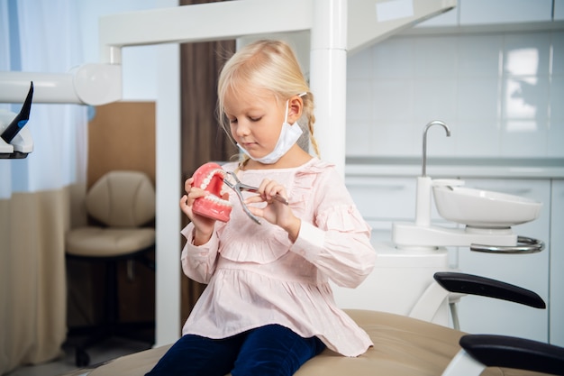 Una dulce niña jugando con una mandíbula artificial e instrumentos médicos en una clínica dental