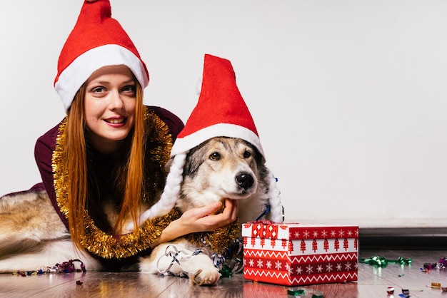 Una dulce niña pelirroja con una gorra roja y con una malla dorada alrededor del cuello camina por el suelo con su perro, esperando el año nuevo 2018.