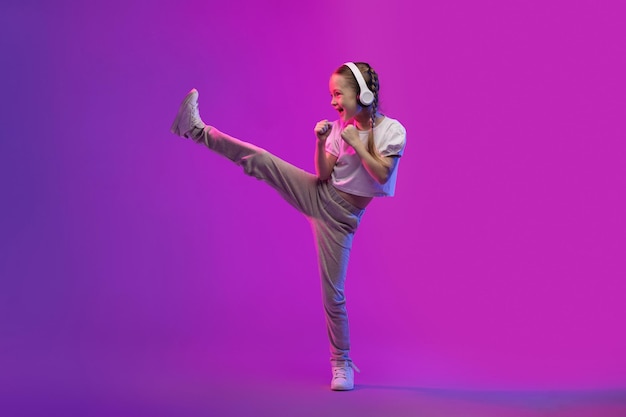 Dulce niña preadolescente usando auriculares inalámbricos y haciendo karate