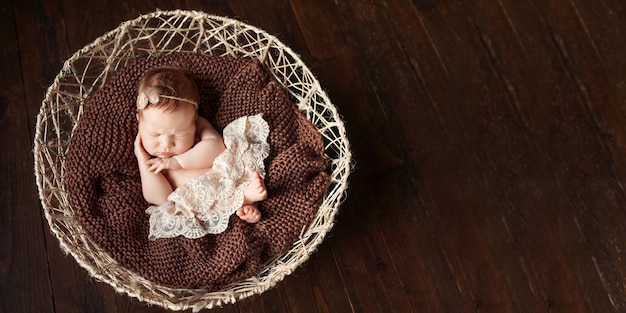 Dulce niña recién nacida duerme en la canasta. Fondo marrón oscuro. Copia espacio