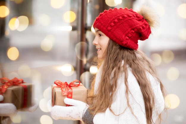 Una dulce niña con un regalo mira por la ventana de la tienda Ambiente navideño de Año Nuevo