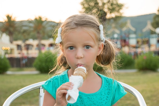 Dulce niña rubia en camiseta verde comiendo su helado