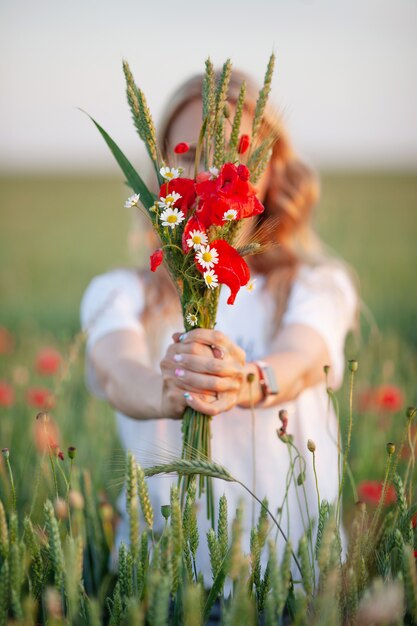 Dulce niña sosteniendo flores de amapola rojas en las manos. Cerca de la foto.