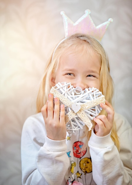 La dulce niña tiene un corazón de San Valentín y piensa en el amor, aislada en un fondo gris