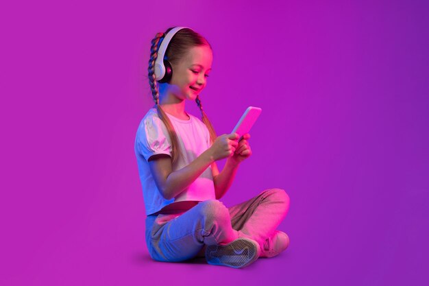 Dulce niña usando teléfono y auriculares sobre fondo luminoso