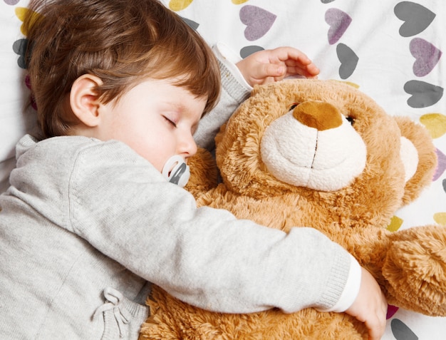 Dulce niño durmiendo con osito de peluche.