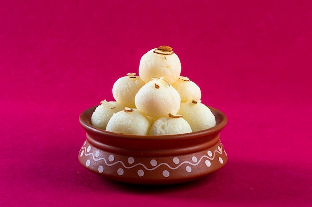 Dulce o postre indio - Rasgulla, famoso dulce bengalí en cuenco de arcilla sobre un fondo rosa.