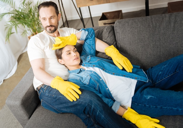 Dulce pareja bastante agotada descansando en el sofá mientras usa guantes y sueña