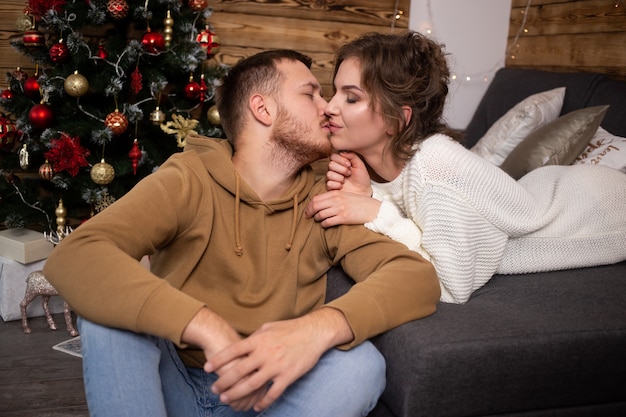 Dulce pareja besándose delante de un árbol de Navidad.