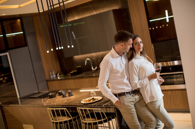 Dulce pareja tomando vino tinto después de una cena romántica en la cocina de lujo