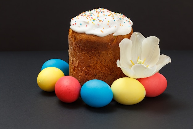 Dulce pastel de Pascua, huevos de Pascua de colores con un capullo de tulipán en la superficie negra