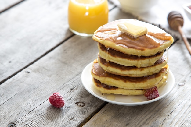 Dulce pila de panqueques caseros con mantequilla, frambuesas y miel para el desayuno