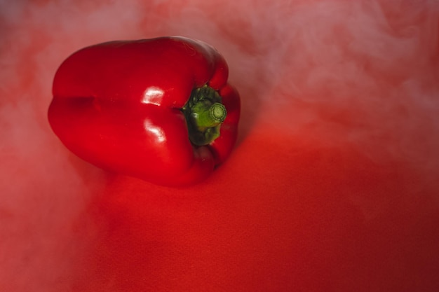 DULCE PIMIENTA ROJA fresca SOBRE FONDO ROJO Con humo alrededor de la foto de pimienta para el menú nutrición adecuada verduras frescas