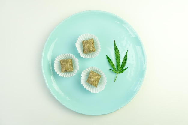 Dulces con aceite de CBD Caramelos coloridos con hojas de cannabis Hoja de marihuana sobre fondo azul ingrediente narcótico en alimentos para relajarse Vista superior plana
