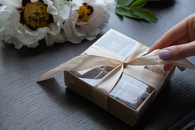 Dulces artesanales de chocolate en caja de regalo con cinta y mano femenina lo abre