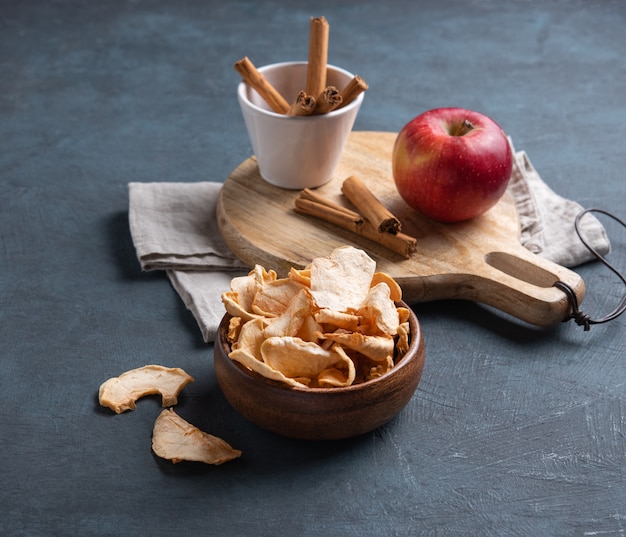 Dulces chips de manzana caseras secas con canela en un tazón de madera sobre fondo azul oscuro