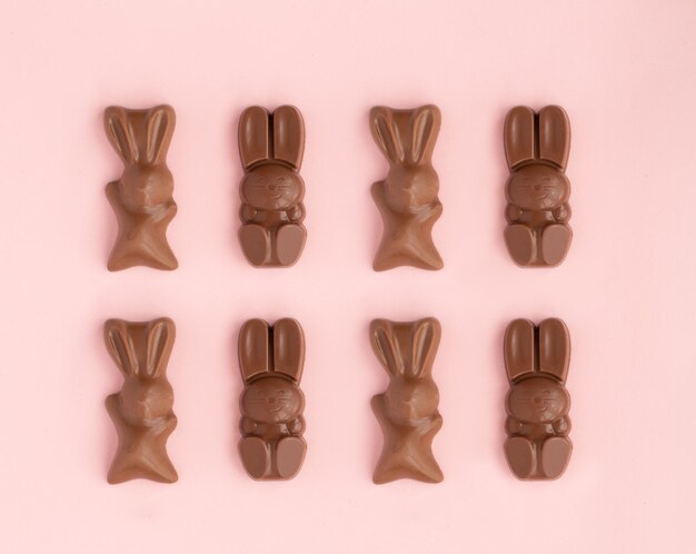 Foto dulces de chocolate con leche en forma de conejito de pascua colocados en filas sobre fondo rosa composición de vacaciones religiosas patrón de conejo para felicitaciones en tarjeta de felicitación símbolo de celebración domingo de cristo