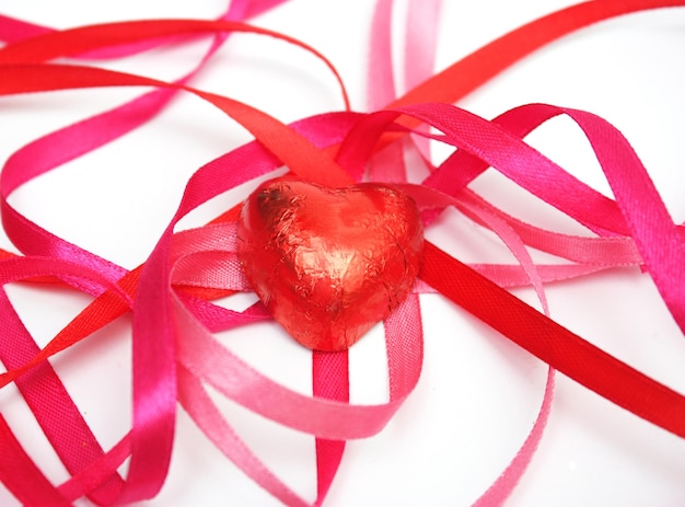 Dulces de concepto de día de San Valentín en lámina roja y cinta de raso rojo Macro disparo aislado sobre fondo blanco