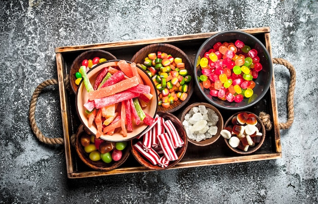 Dulces dulces, frutas confitadas con malvavisco y gelatina en una bandeja de madera. Sobre un fondo rústico.