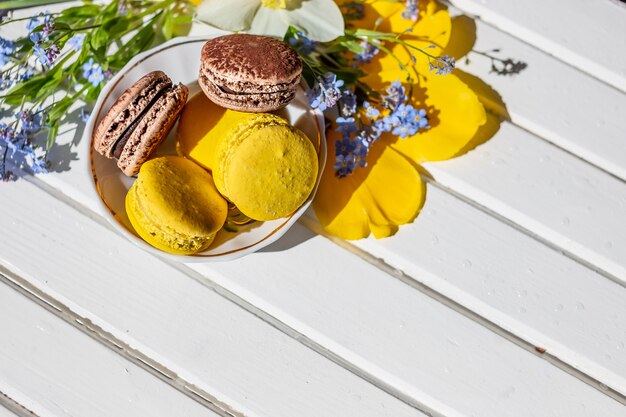 Los dulces franceses de los macarrones y las flores de la oferta florecen en fondo de madera.