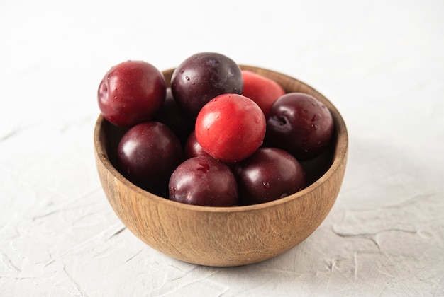 Dulces frescas ciruelas rojas deliciosas en tazón mesa de madera blanca frutas de verano