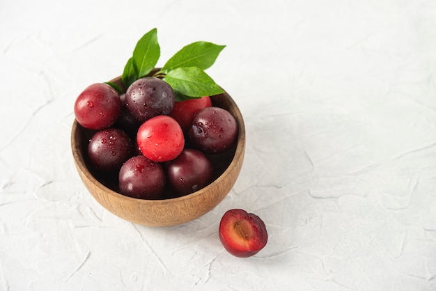 Dulces frescas ciruelas rojas deliciosas en tazón mesa de madera blanca frutas de verano