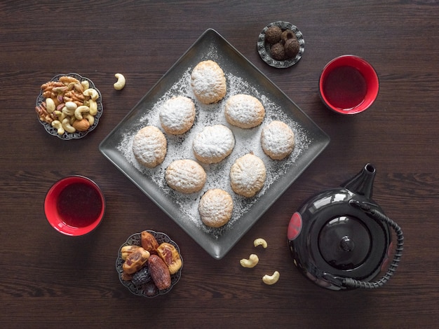 Los dulces hechos a mano del Ramadán se sirven con té en la mesa de madera oscura. Galletas egipcias "Kahk El Eid" - galletas de la Fiesta Islámica de El Fitr. Vista superior