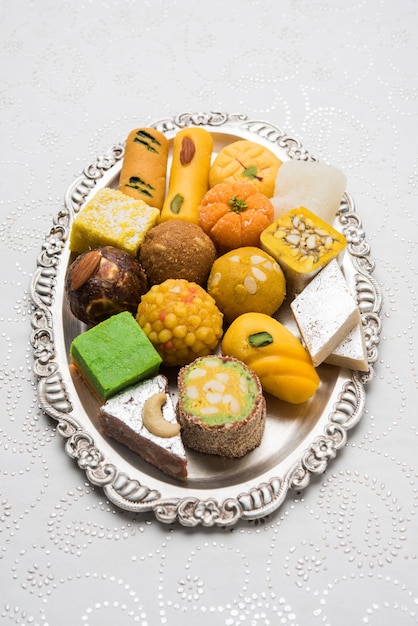 Dulces indios servidos en plato de madera o plata. Variedad de Peda, burfi, laddu en placa decorativa, enfoque selectivo