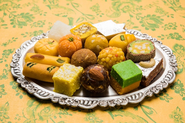 Dulces indios servidos en plato de madera o plata. Variedad de Peda, burfi, laddu en placa decorativa, enfoque selectivo