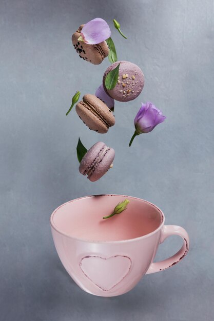 Dulces macarons franceses caen mezclados con flores en una taza rosa vacía