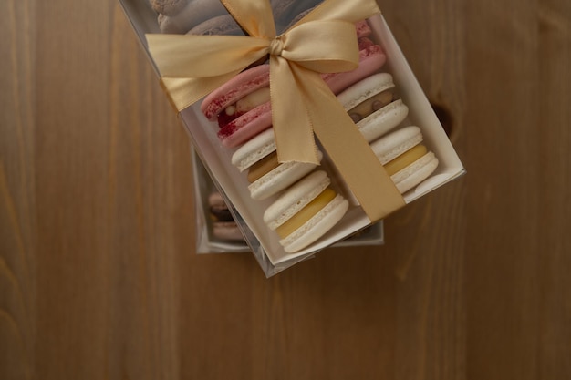 Dulces macarrones de postre en una caja decorada con una cinta sobre una mesa de madera