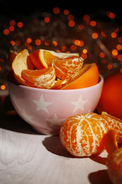 Foto dulces mandarinas y naranjas en la mesa en un tazón sobre fondo de luces de navidad