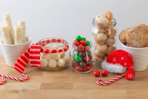 Dulces de Navidad y galletas en frascos en estante de madera sobre fondo blanco.