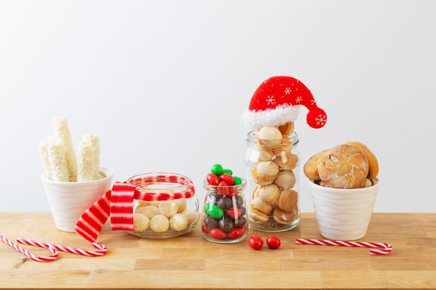 Dulces de Navidad y galletas en frascos en estante de madera sobre fondo blanco.