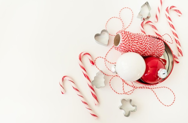 Dulces navideños junto con cortadores de galletas Juguetes para árboles de Navidad e hilo rojo para envolver regalos yacen sobre una mesa blanca Ruido de enfoque selectivo Navidad y Año Nuevo 20232024