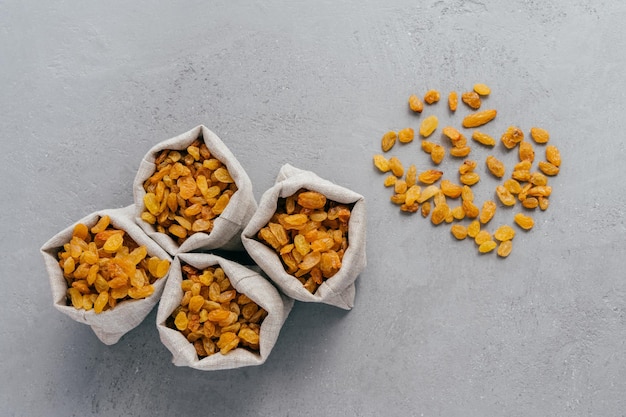 Dulces pasas secas en sacos de arpillera aisladas sobre fondo gris Espacio de copia Frutas secas sabrosas para la venta Bayas saludables para comer