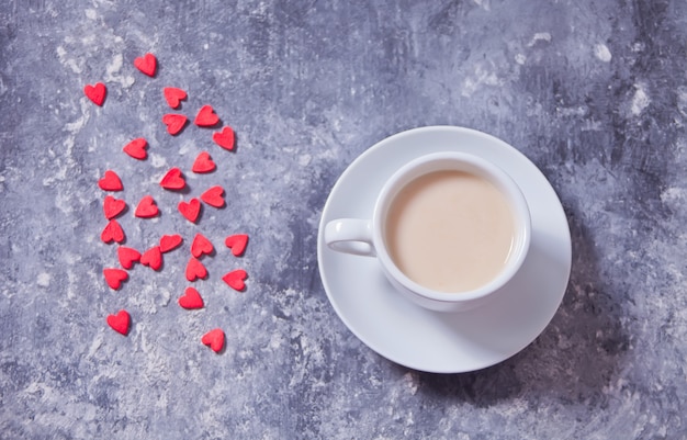 Dulces rojos en forma de corazón y una taza de café sobre un fondo de hormigón