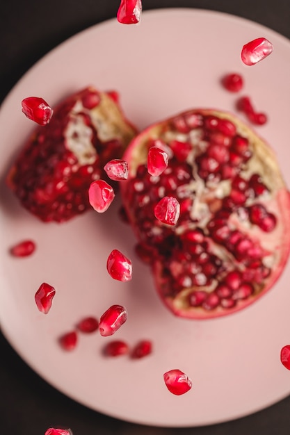 Dulces sabrosas semillas de granada agria que vuelan sobre un plato rosa con fruta pelada